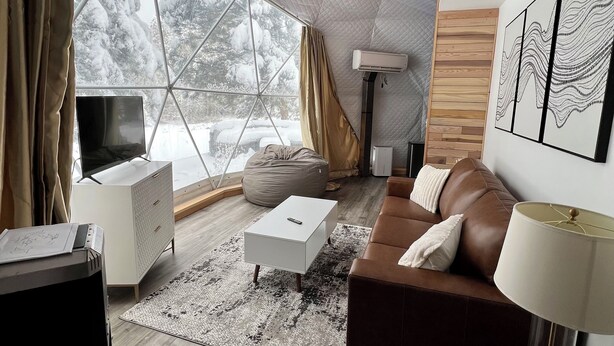 Un salon moderne avec une grande fenêtre, un canapé blanc, une table basse et un téléviseur posé sur un meuble.