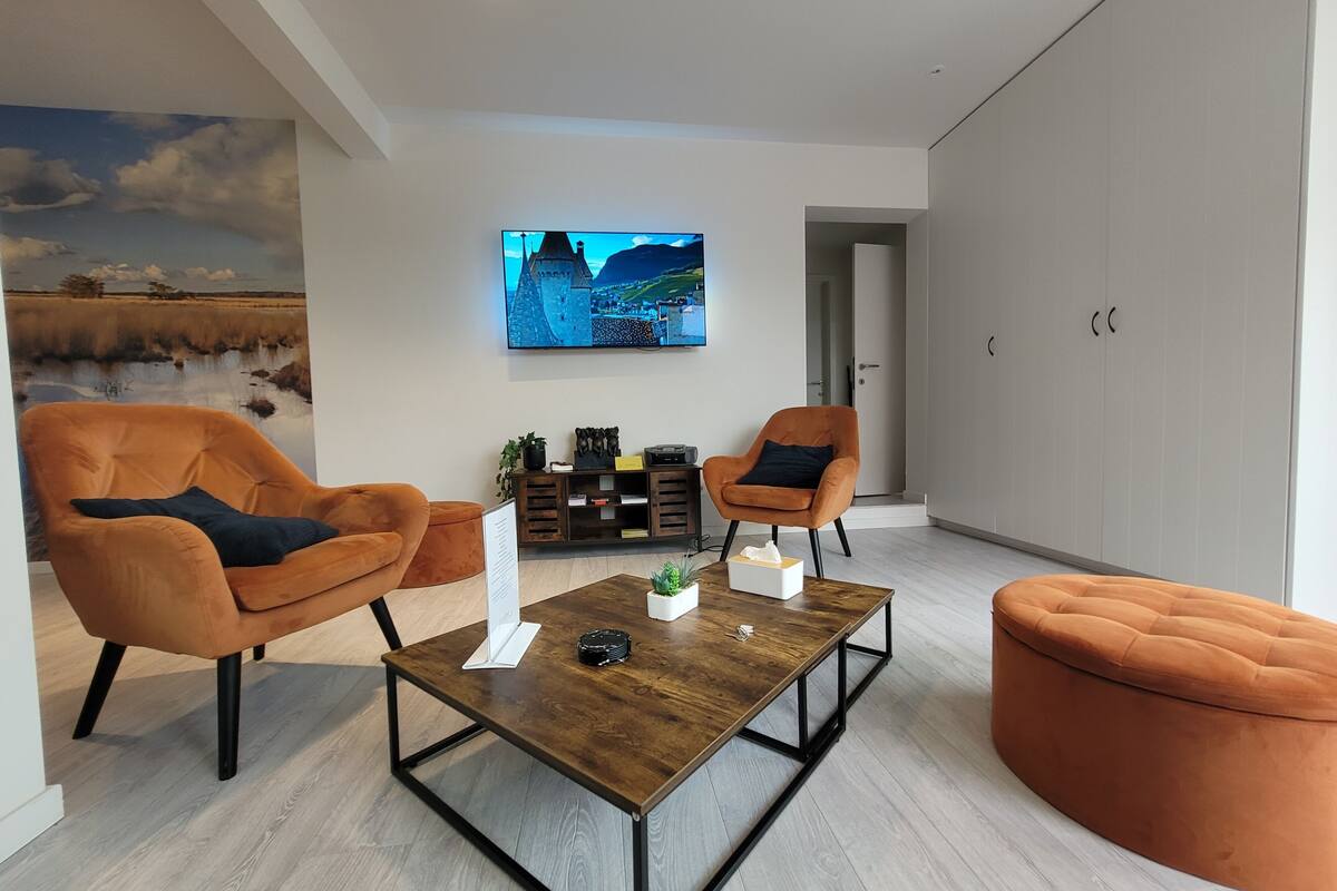 A modern living room with two orange armchairs, a wooden coffee table, and a television mounted on the wall.