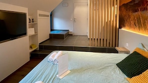 A modern hotel room with a bed, a TV, a small seating area, and a staircase leading to an upper level. - b&b d'Ereplatse (Zuienkerke)