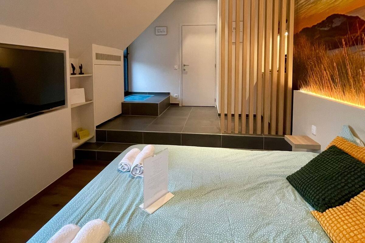 A modern hotel room with a bed, a TV, a small seating area, and a staircase leading to an upper level.