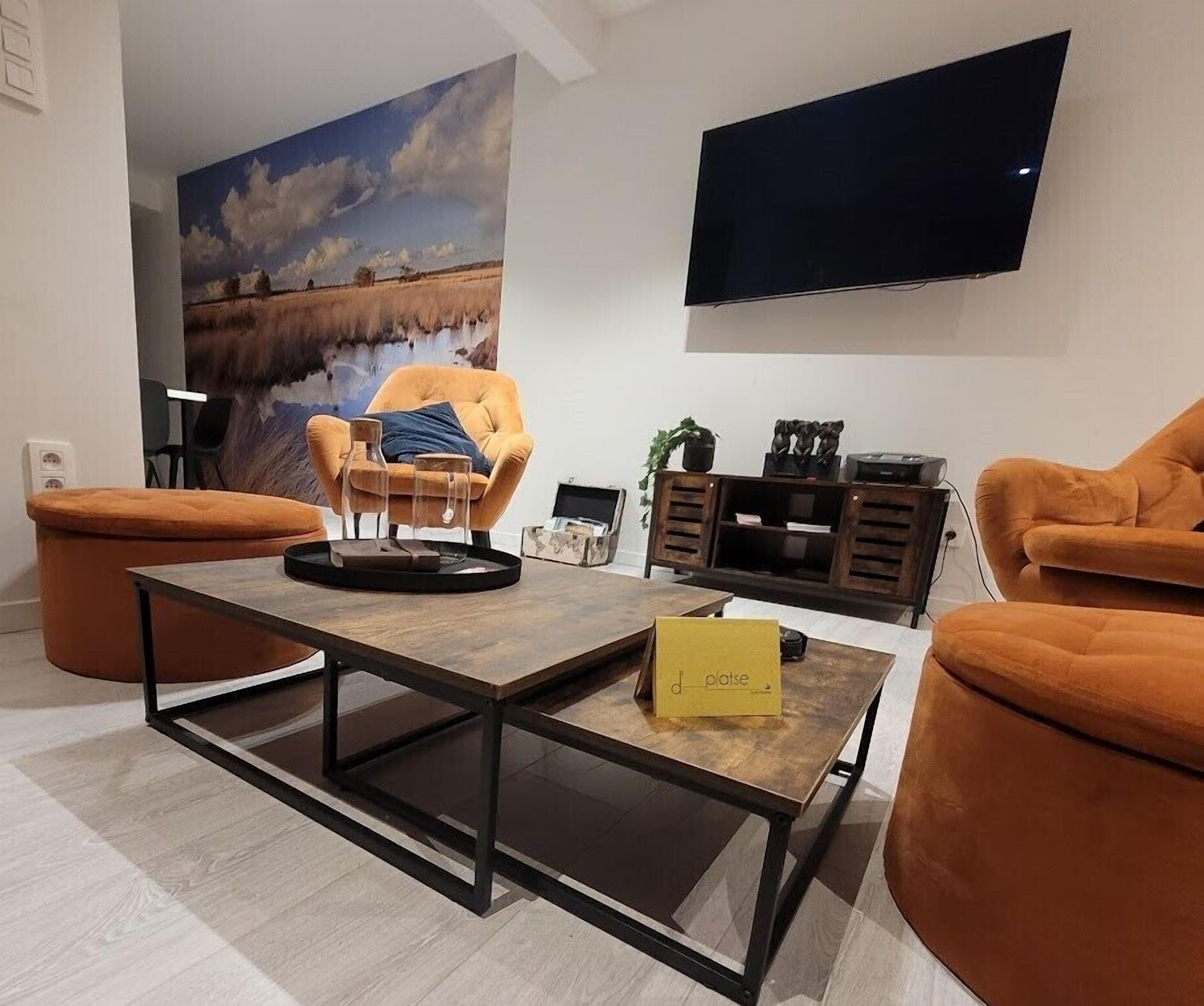 Una sala de estar moderna con un cuadro grande, un televisor de pantalla plana y muebles color naranja.