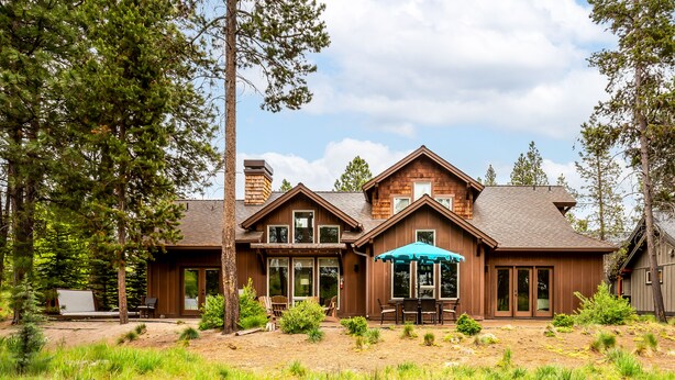 A two-story log cabin with a patio area, large windows, and a covered outdoor seating area. - TRAI39 - Stunning Caldera Springs Home (Sunriver)