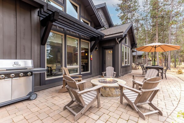 A patio with Adirondack chairs, a fire pit, and a grill.