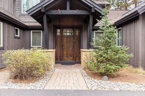 A wooden front door with a stone ledge, a small tree, and a gravel pathway leading to the entrance.