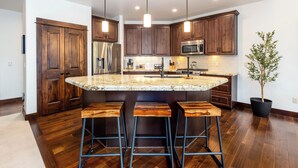 A modern kitchen with wooden cabinets, a stainless steel refrigerator, a microwave, and a large island with bar stools. - TRAI39 - Stunning Caldera Springs Home (Sunriver)