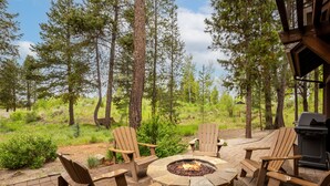 A circular fire pit surrounded by wooden Adirondack chairs in a forested outdoor area. - TRAI39 - Stunning Caldera Springs Home (Sunriver)