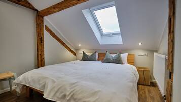 A bedroom with a skylight, wooden beams, a bed with pillows, a bedside table, and a radiator.
