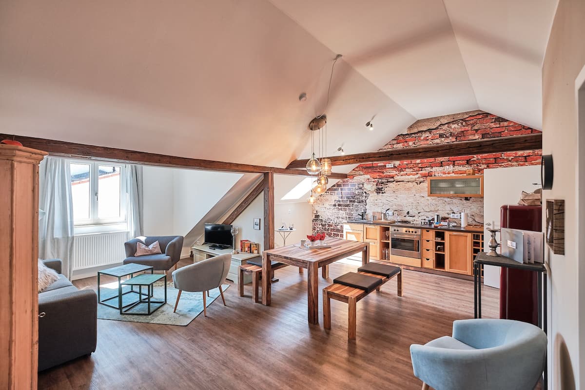 A spacious living area with a wooden floor, a dining table, and a kitchen in the background.