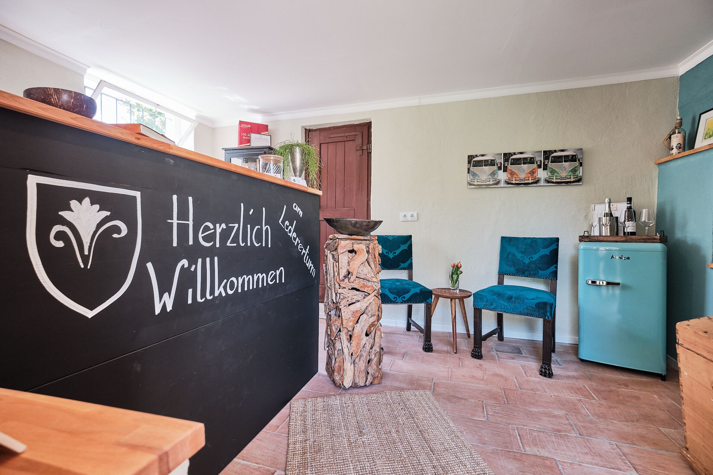 Ein Empfangsbereich mit einer Tafel, auf der 'Herzlich Willkommen' steht, und einem blauen, alten Kühlschrank.