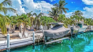 Un port de plaisance avec des bateaux amarrés, un espace piscine avec des chaises longues et des palmiers.