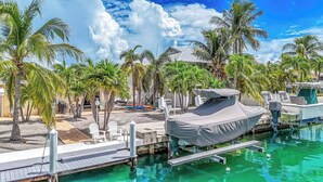Un port de plaisance doté d’un abri pour bateaux, d’un quai et d’un espace piscine avec des chaises et des palmiers.