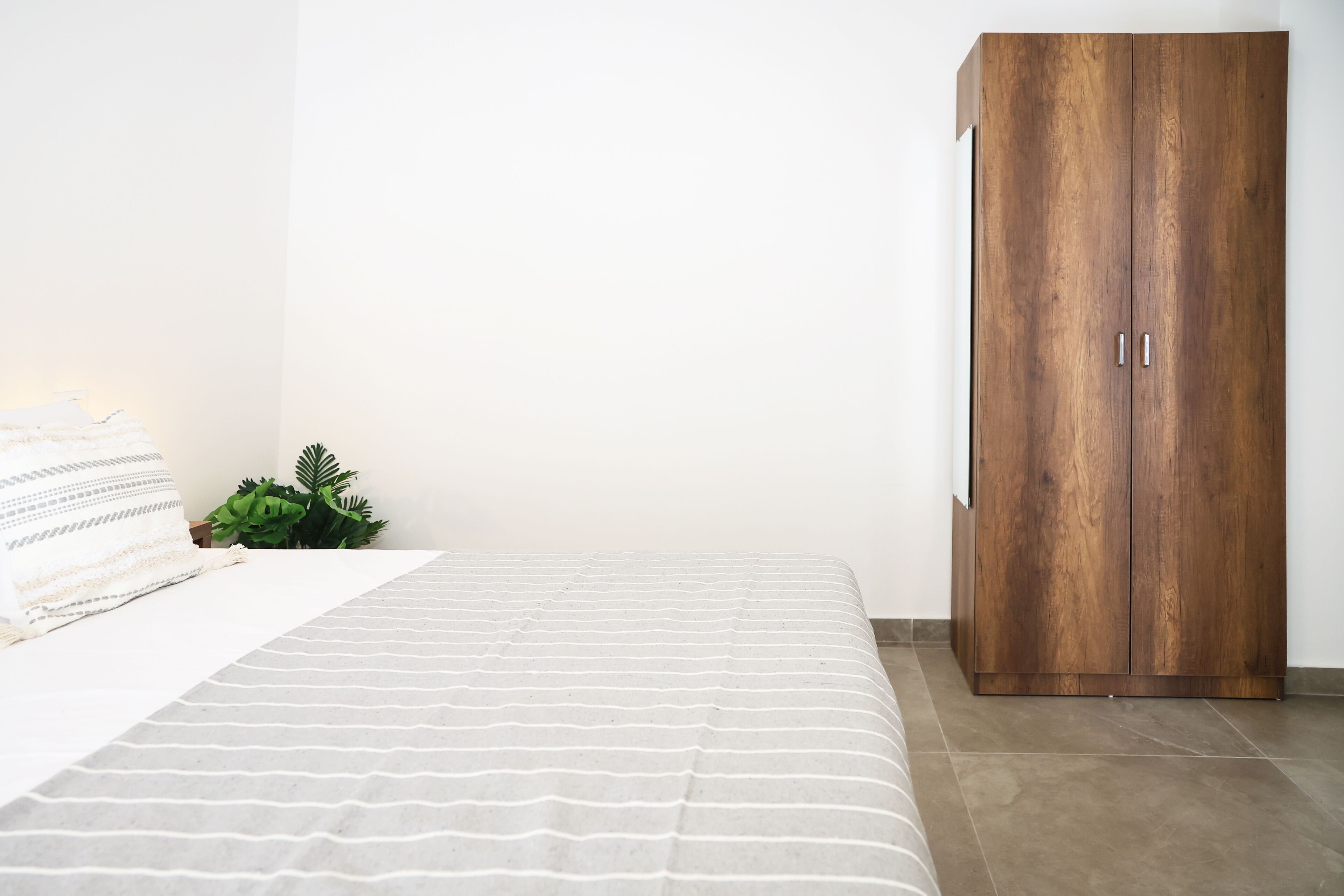 Ein Schlafzimmer mit einem Bett, einem Holzschrank, einer Topfpflanze und einer weißen Wand.