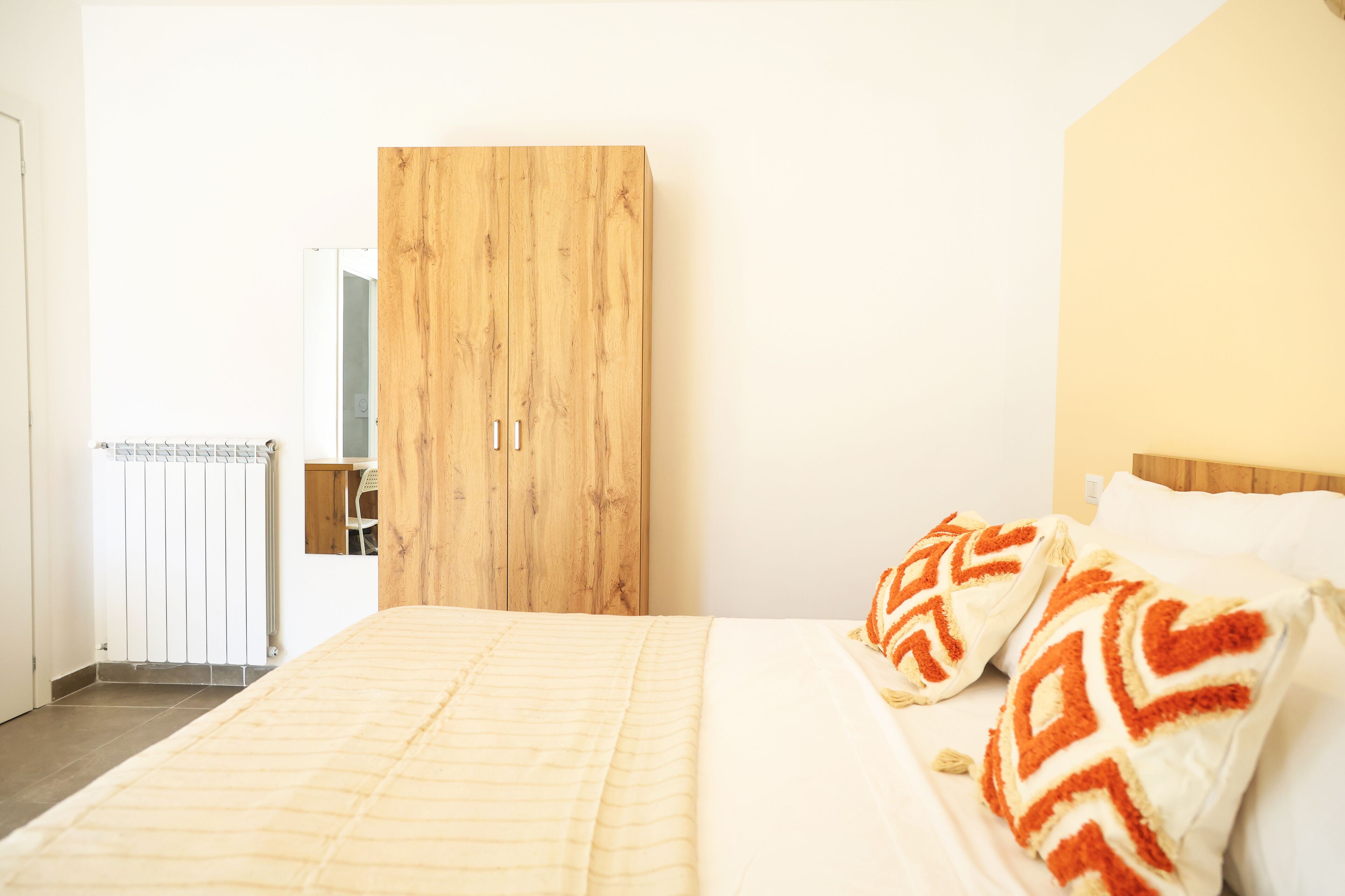 A bedroom with a bed, wooden wardrobe, and a radiator.