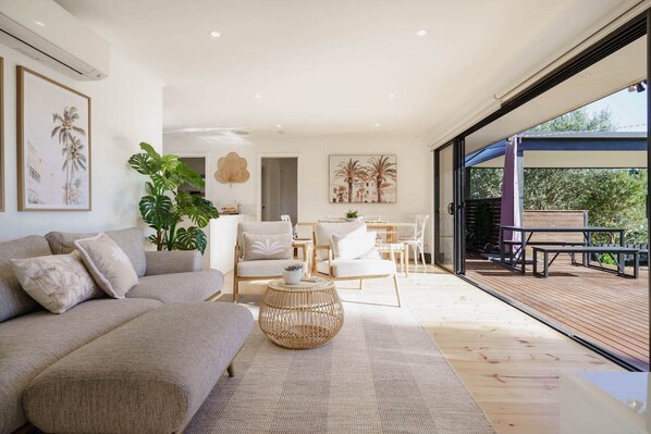 A spacious living area with a sofa, coffee table, and chairs, a dining area with a table and chairs, and a wooden deck with outdoor seating.