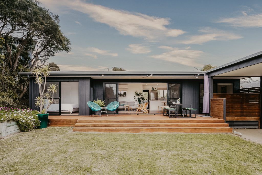 A modern house with a patio, outdoor seating, and a view of the backyard.