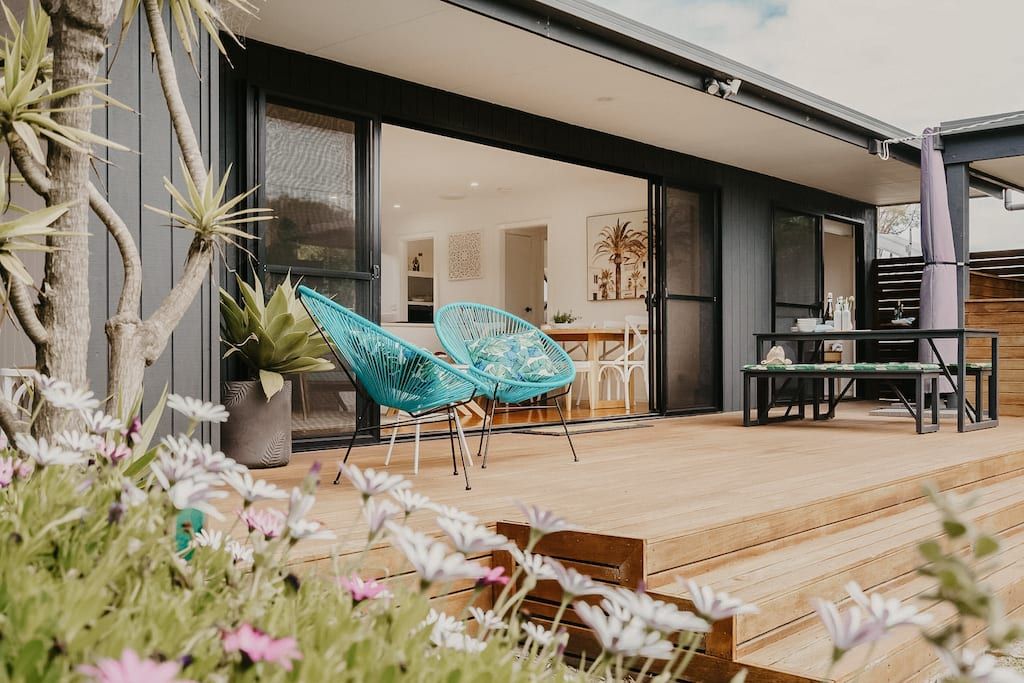 A modern outdoor patio with a wooden deck, two blue woven chairs, a table, and a dining area.