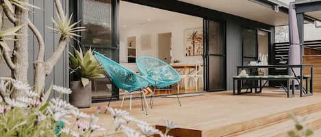 A modern outdoor patio with a wooden deck, two blue woven chairs, a table, and a dining area.