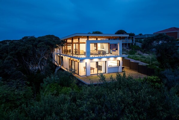 A modern two-story house with large glass windows and a balcony.