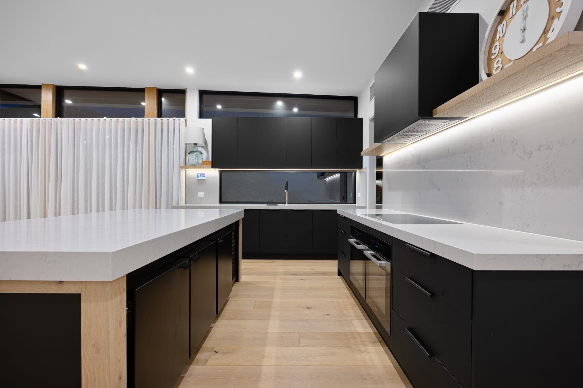 A modern kitchen with dark cabinetry, white countertops, and a wooden floor.