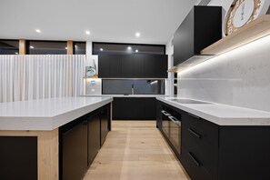 A modern kitchen with dark cabinetry, white countertops, and a wooden floor.