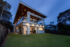 A modern two-story house with a balcony, large windows, and a well-maintained lawn.