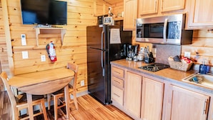A wooden-paneled kitchen with a refrigerator, microwave, and a television mounted on the wall. - Cozy Lake Front Park Model on Douglas Lake with Hot Tub! (Dandridge)