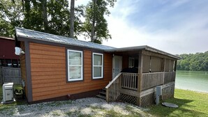 A small wooden cabin with a deck, a gravel driveway, and a lake view. - Cozy Lake Front Park Model on Douglas Lake with Hot Tub! (Dandridge)