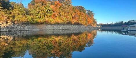 A calm lake with autumn foliage reflecting on the water, a dock, and a building in the background.