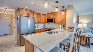 Una cocina moderna con armarios de madera, electrodomésticos de acero inoxidable, encimera de mármol e iluminación colgante.