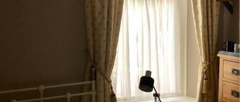 Un dormitorio con cama, mesita de noche con lámpara, cómoda y ventana con cortinas.