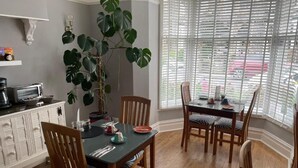 A dining area with a table and chairs, a potted plant, and a window with blinds. - Glendale Guest House (Keswick)