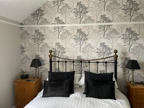 A bedroom with a bed, two nightstands, and a wall with a tree pattern. - Glendale Guest House (Keswick)