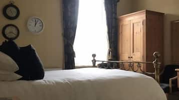 A bedroom with a bed, a wardrobe, a clock, and a window with curtains.