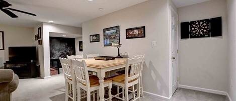 A dining area with a wooden table and white chairs, a ceiling fan, recessed lighting, and framed artwork on the walls.