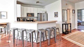 A modern kitchen with white cabinets, stainless steel appliances, and a bar area with stools. - Comfortable 4 bedroom Townhome in Excellent Location, Bear Trap Dunes Community! Community Pool, Shuttle Service, WIFI, Golf, and more! (Ocean View)