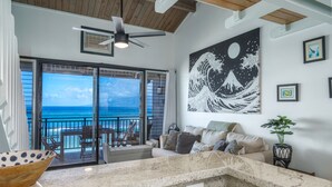 A spacious living area with a view of the ocean, a ceiling fan, a large artwork, and a bowl on the counter. - Beautiful Beachfront Bungalow (Lahaina)