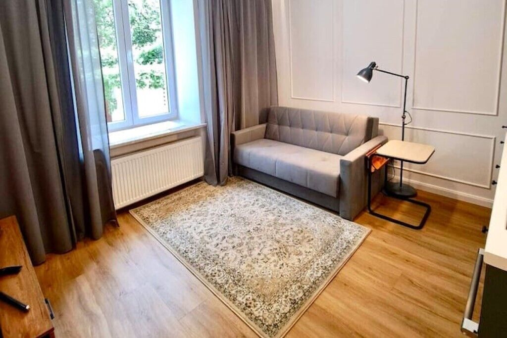 A modern living room with a sofa, a small table, a floor lamp, and a large window with curtains.