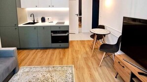 En kompakt opholdsstue med tekøkken, spiseplads og tv.