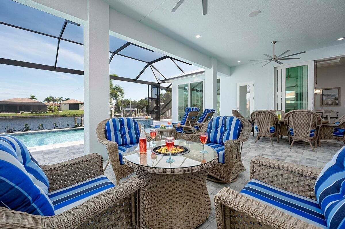 Un área de estar al aire libre cubierta con muebles de mimbre y una mesa de cristal, con vista a una piscina y una extensión de agua.
