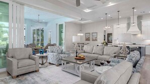 A spacious living room with a large sofa, a coffee table, and a dining area with a chandelier. - Mystique  - Luxury Waterfront Home (Cape Coral)
