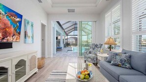 A modern living room with a sofa, a coffee table with fruit, a TV, and artwork on the wall. - Mystique  - Luxury Waterfront Home (Cape Coral)