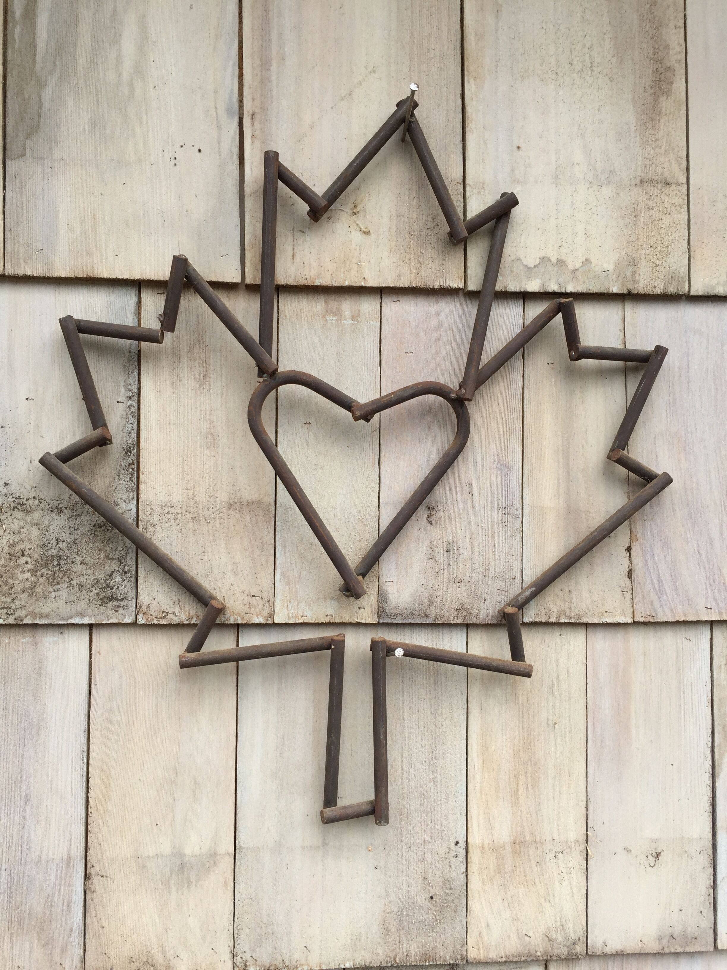 A maple leaf-shaped metal sculpture mounted on a wooden wall.