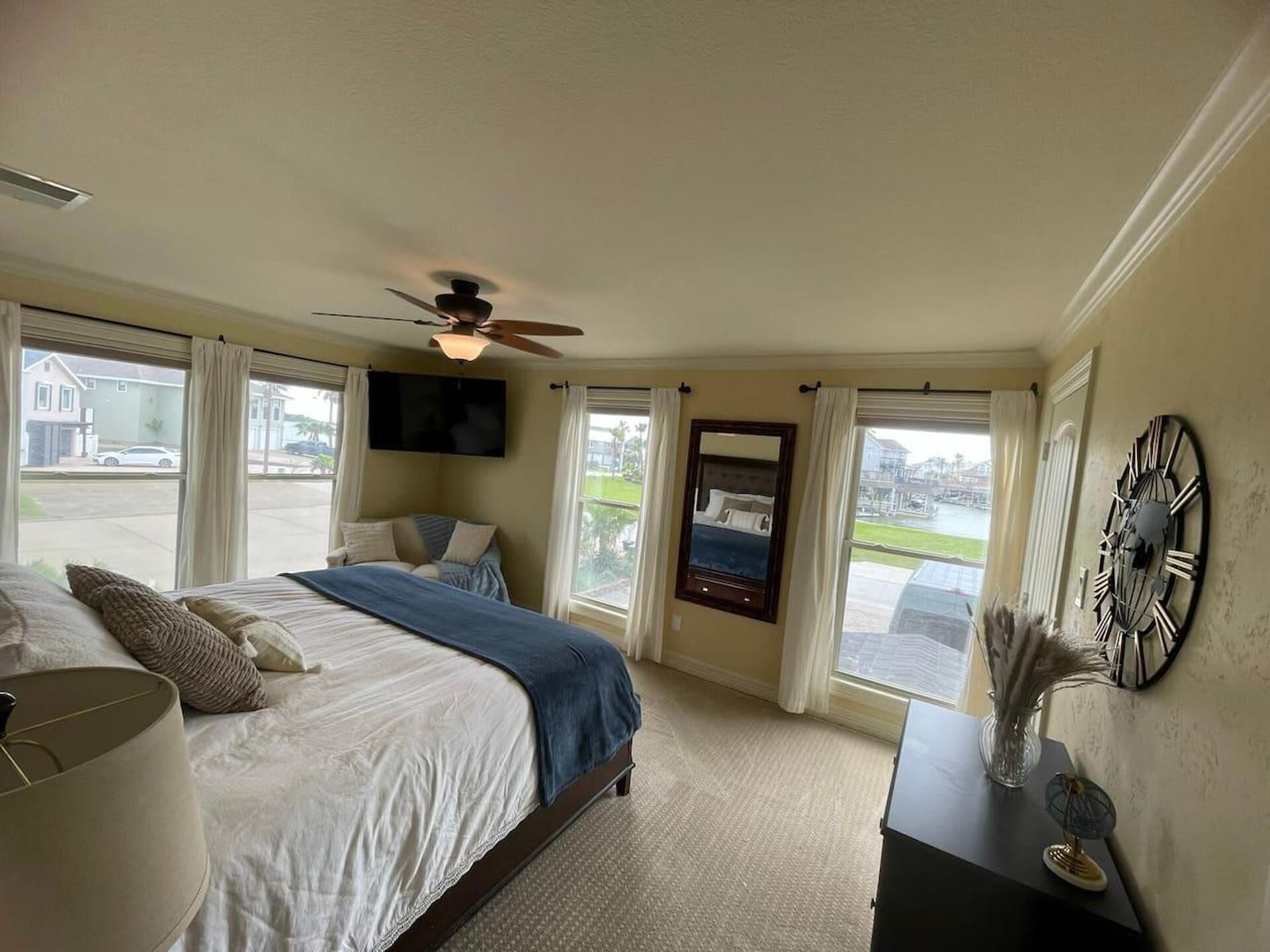 A bedroom with a bed, a ceiling fan, a TV, and a view of the outside.