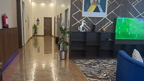 A hotel lobby with a marble floor, a reception desk, a blue sofa, and a mounted TV. - Smayah Hotel (Riyadh)
