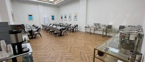 A conference room with multiple tables and chairs, a coffee station, and a glass display case with items.