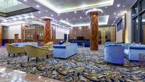 A spacious lobby with a marble-patterned carpet, blue sofas, and wooden pillars. - Smayah Hotel (Riyadh)