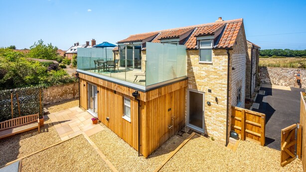 A modern house with a wooden deck, a glass-enclosed patio, and a stone exterior. - May Cottage Titchwell, Norfolk (Titchwell)