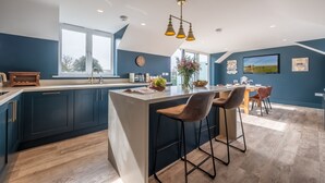A modern kitchen with a central island, bar stools, and a dining area with a table and chairs. - May Cottage Titchwell, Norfolk (Titchwell)