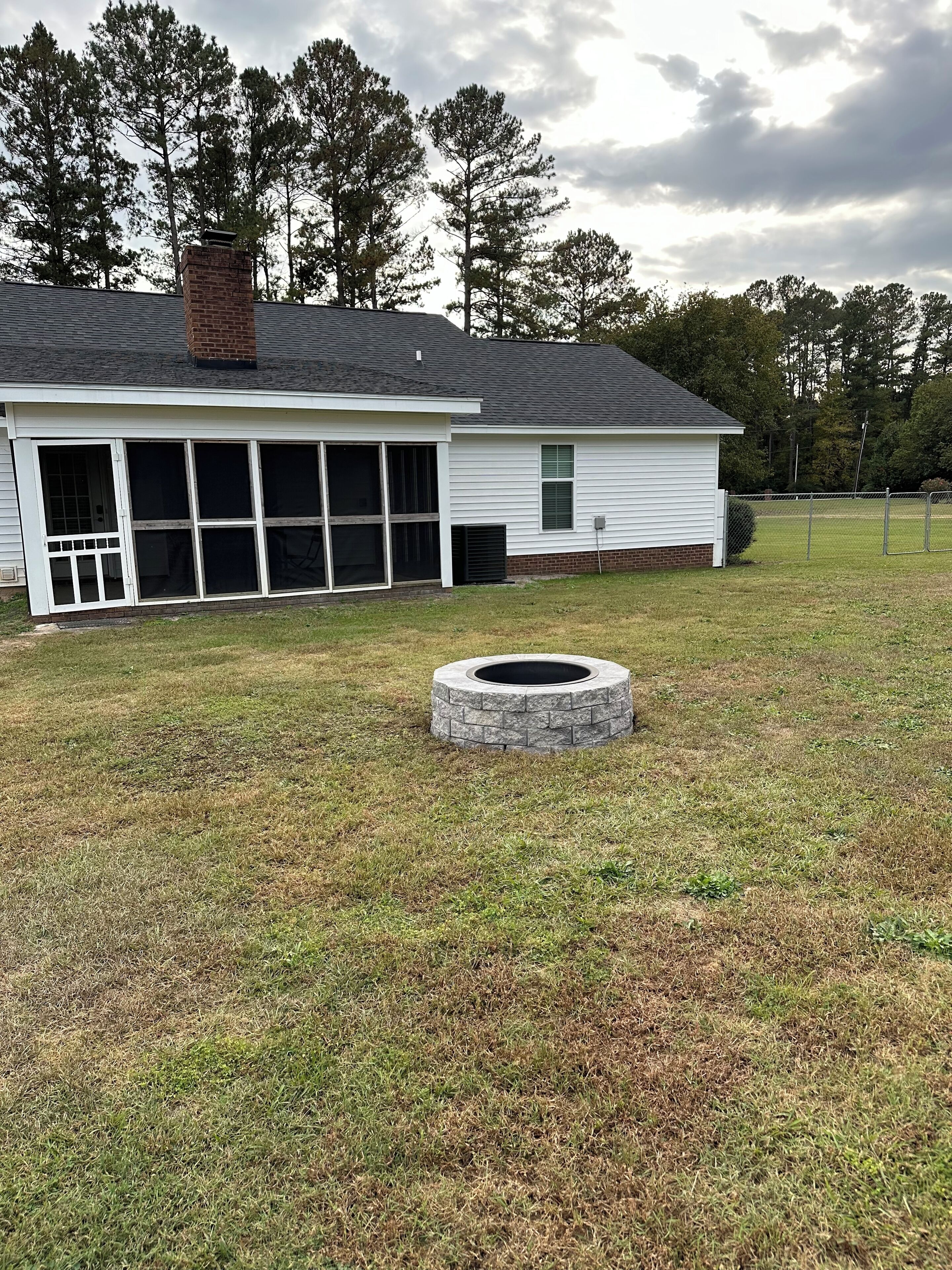 A single-story house with a covered patio and a stone fire pit in the yard.