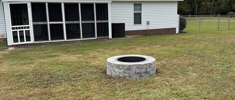 A single-story house with a covered patio and a stone fire pit in the yard.